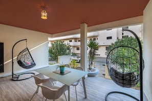 A balcony with a table, chairs, hanging chairs, and potted plants. - Coastal Escape •Steps to Beach •Pool • Inema Lagos (Lagos)