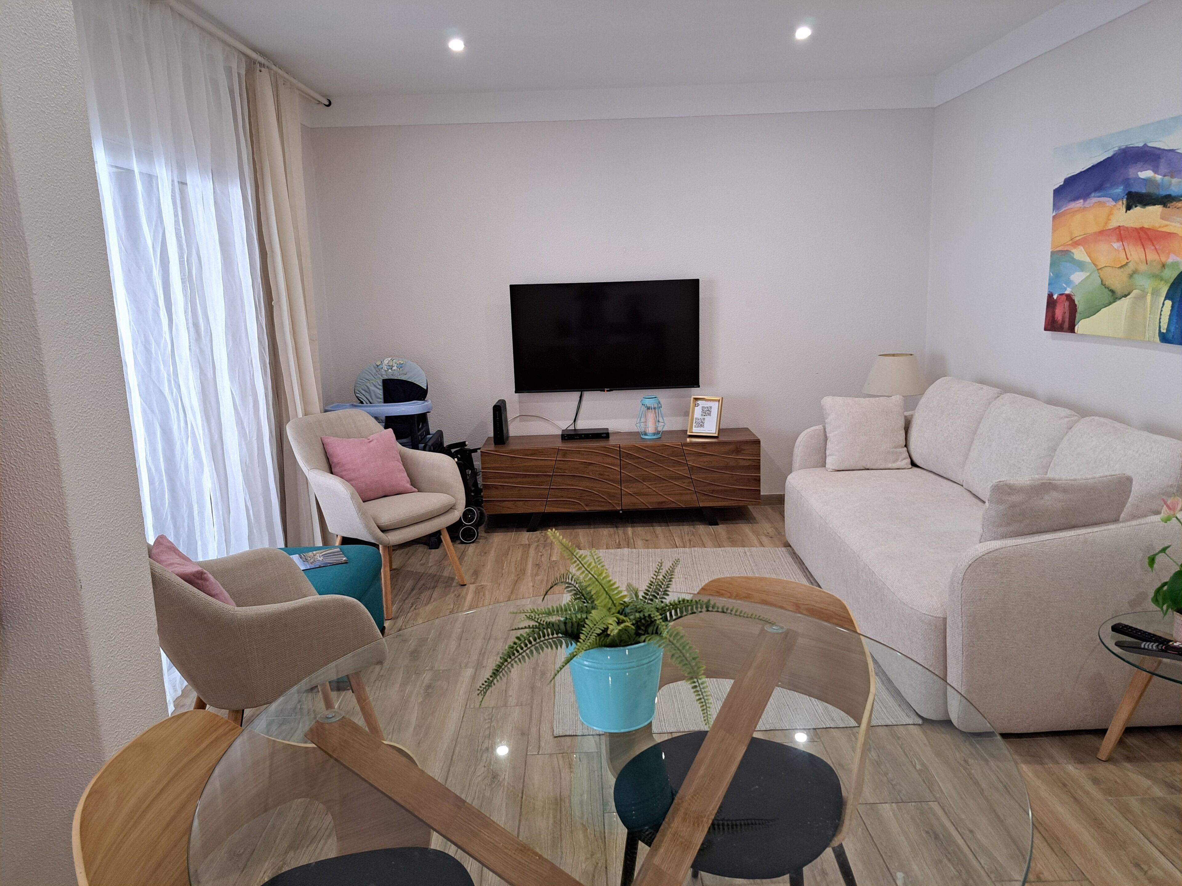 Ein modernes Wohnzimmer mit einer Couch, Sesseln, einem Couchtisch, einem Fernseher und einem Bild an der Wand.