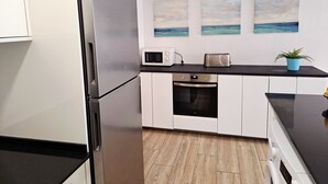 Een moderne keuken met roestvrijstalen apparatuur, witte kastjes, een zwart aanrecht en uitzicht op de oceaan via een kunstwerk.