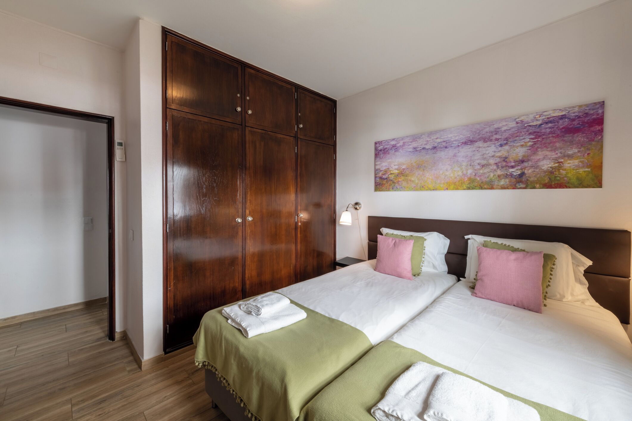 Une chambre d’hôtel avec une grande armoire, un lit avec plusieurs oreillers et un tableau au mur.