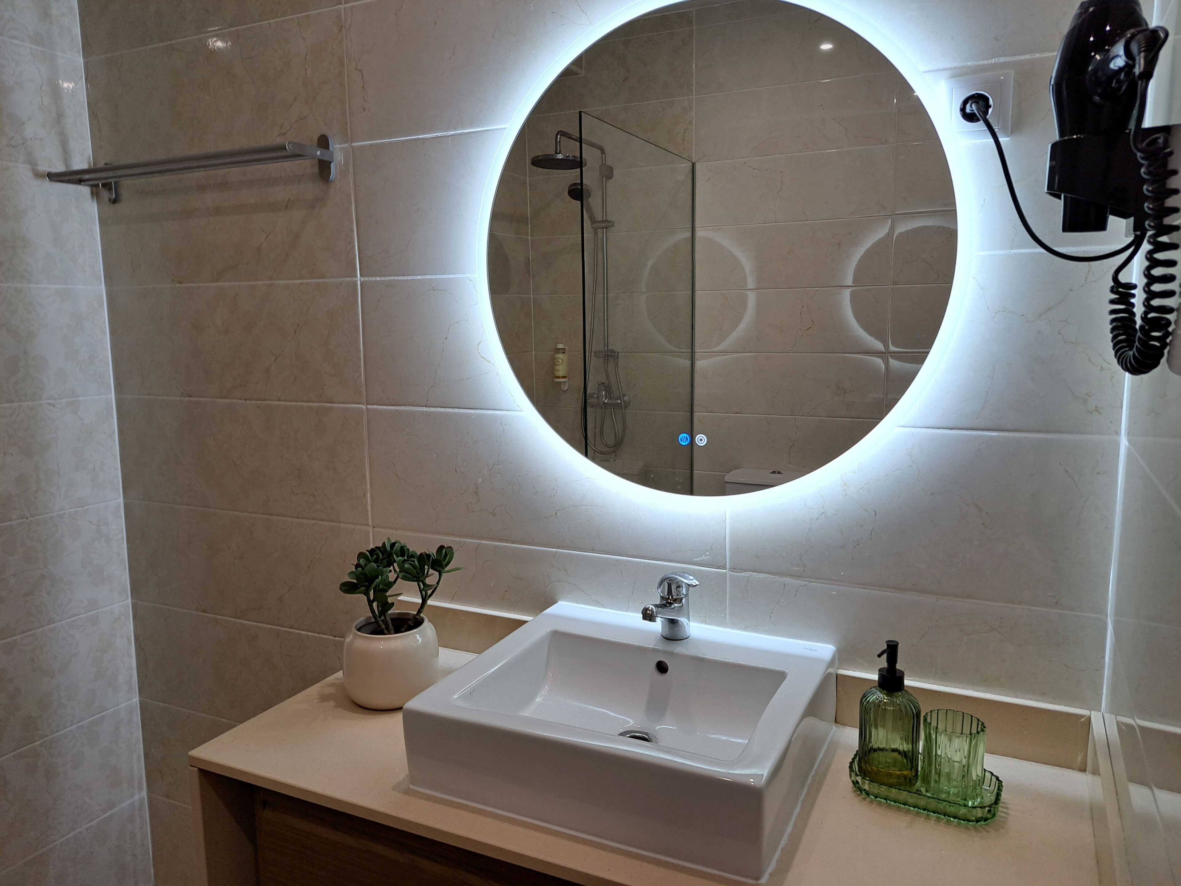 Une salle de bain avec un miroir rond, un lavabo, un porte-serviettes et une plante en pot.
