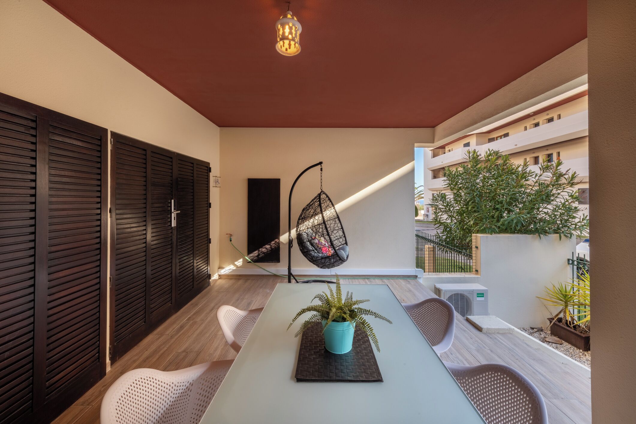 A modern outdoor seating area with a table, chairs, a hanging chair, and a potted plant.