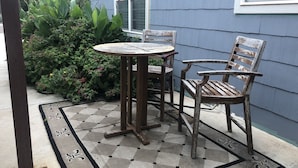 Um pátio com uma mesa redonda e duas cadeiras de madeira, com um tapete quadriculado ao redor.