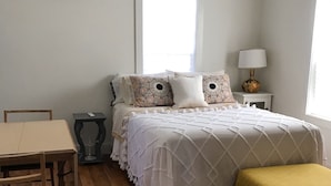 Quarto com cama, mesa de cabeceira, abajur e janela.