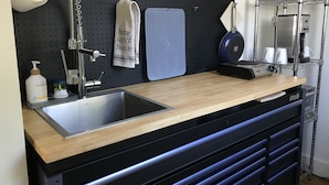 Uma cozinha com um painel de rolhas preto, bancada de madeira, pia e máquina de café.