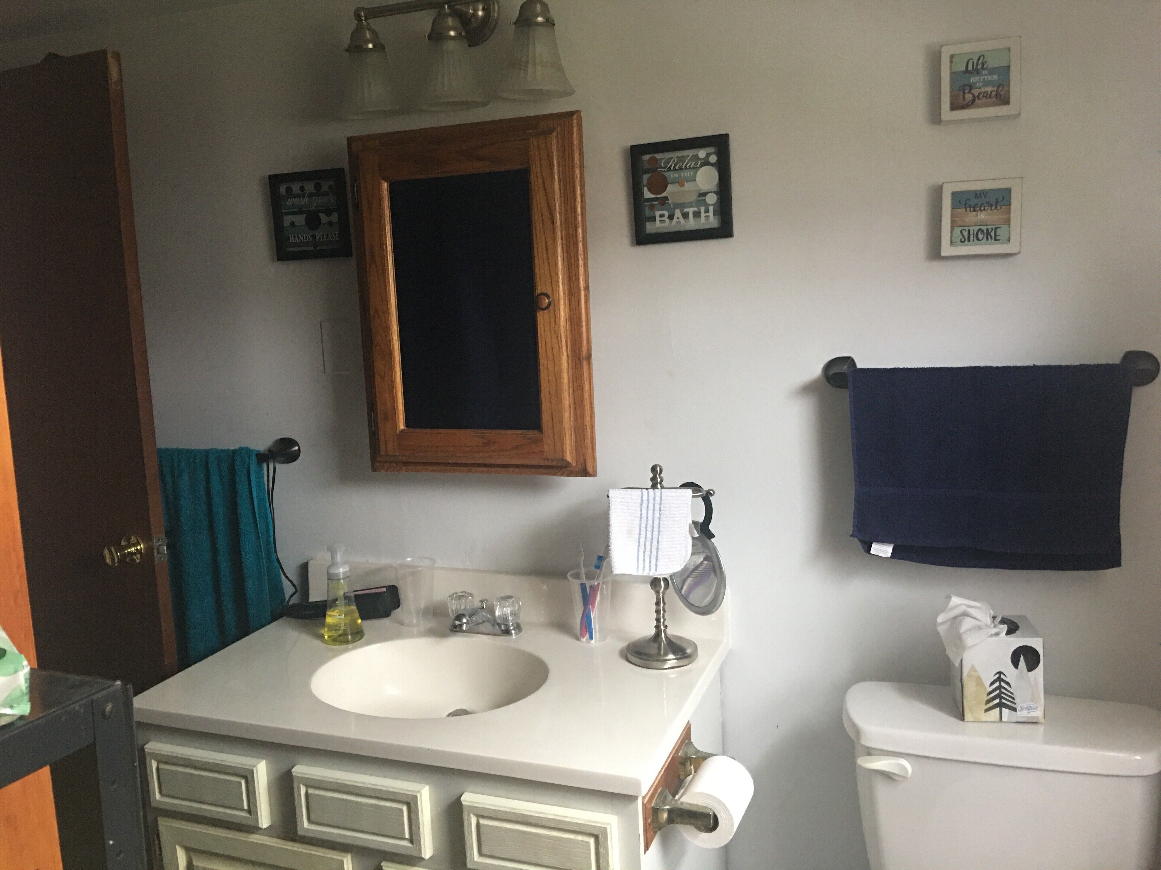 Un bagno con un lavandino bianco, un pensile in legno, un portasci con un asciugamano blu e un water.