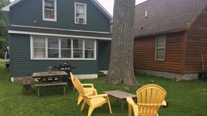 Un jardin avec une table de pique-nique, deux chaises jaunes et un barbecue.