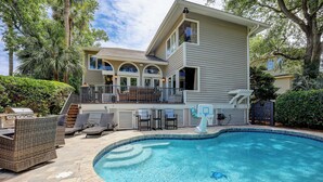 A two-story house with a swimming pool, outdoor furniture, and a basketball hoop.