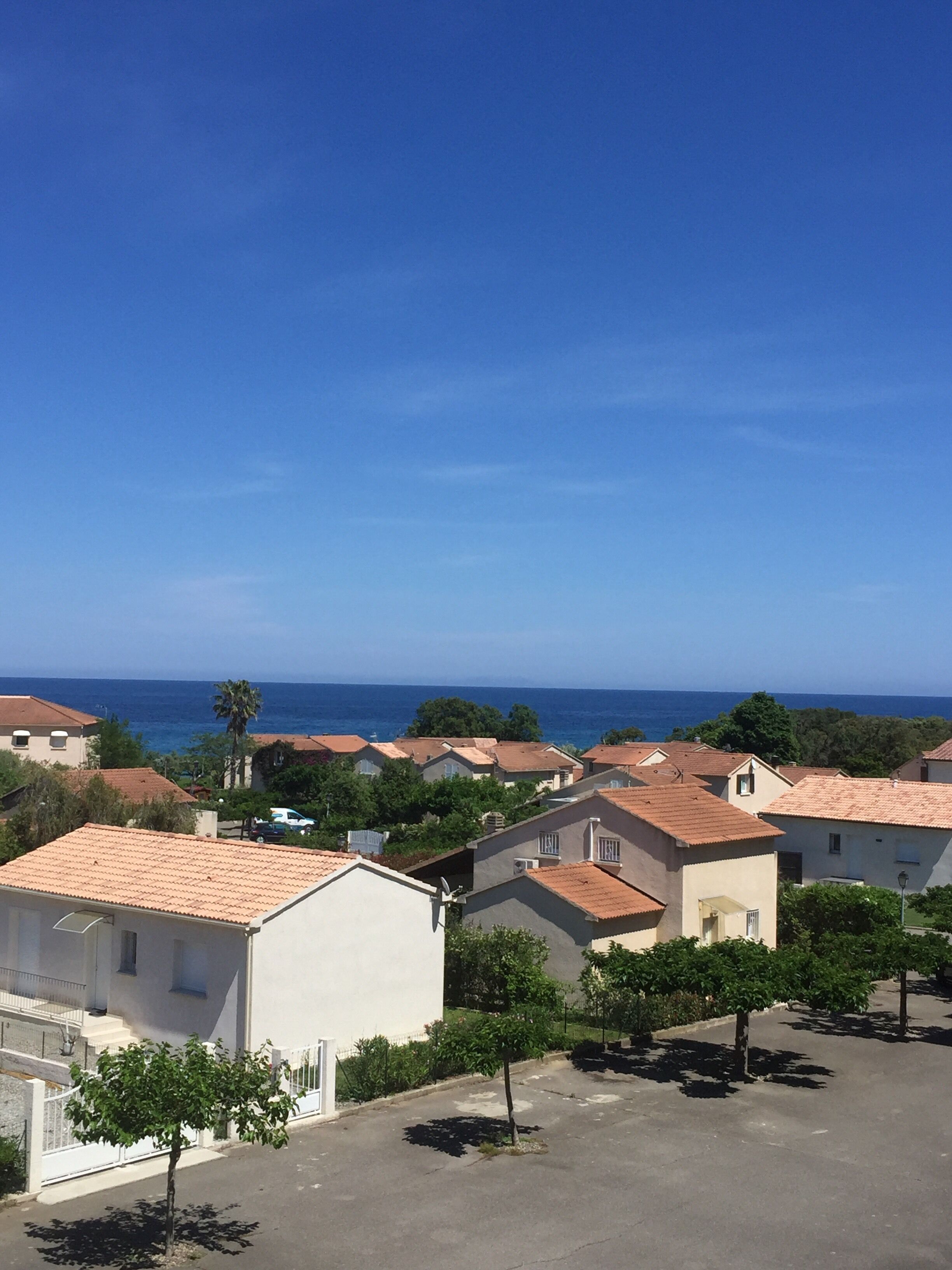 A coastal residential area with houses, a clear blue sky, and the sea in the background.