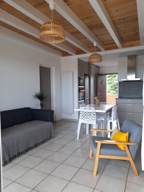 A modern living space with a sofa, dining table, chairs, and a kitchen area.