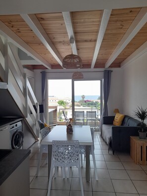A modern living room with a dining area, a washing machine, and a view of the sea.