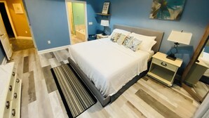 A bedroom with a bed, bedside tables, a nightstand, a lamp, a painting, and a door leading to a bathroom. - Newly renovated modern, spacious & quiet location (Panama City)