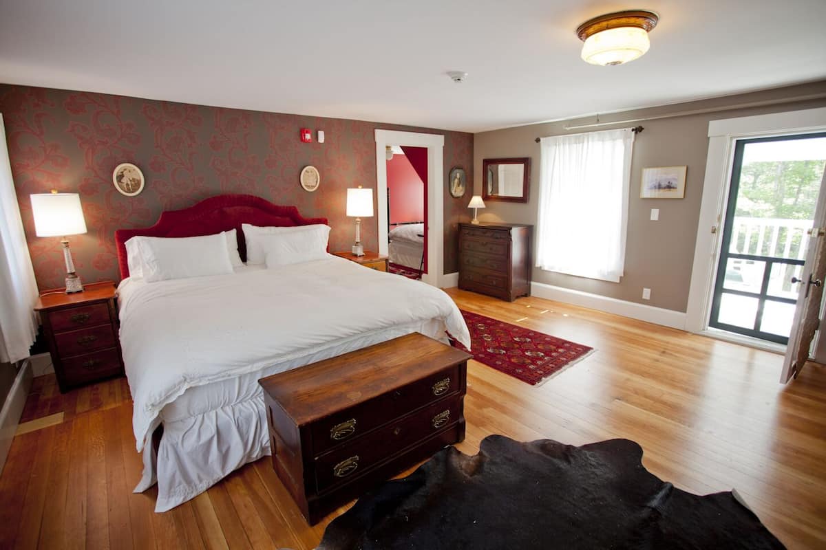A bedroom with a large bed, wooden nightstands, a dresser, a red rug, and a black leather piece on the floor.