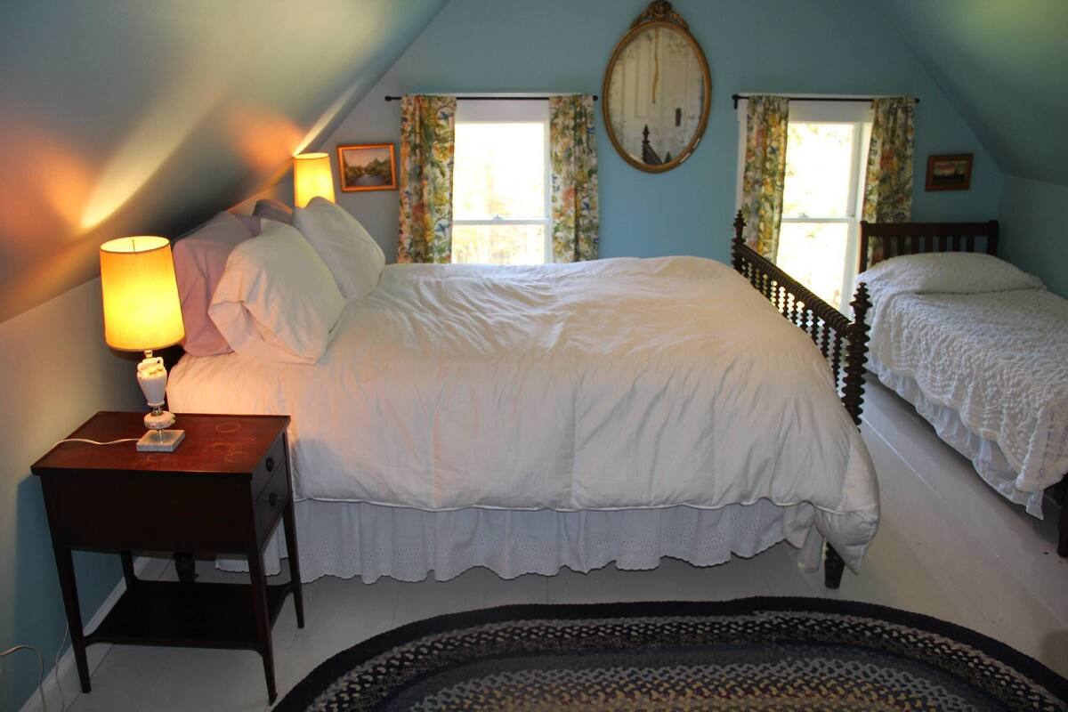 A bedroom with a single bed, a nightstand, a lamp, and a window with curtains.