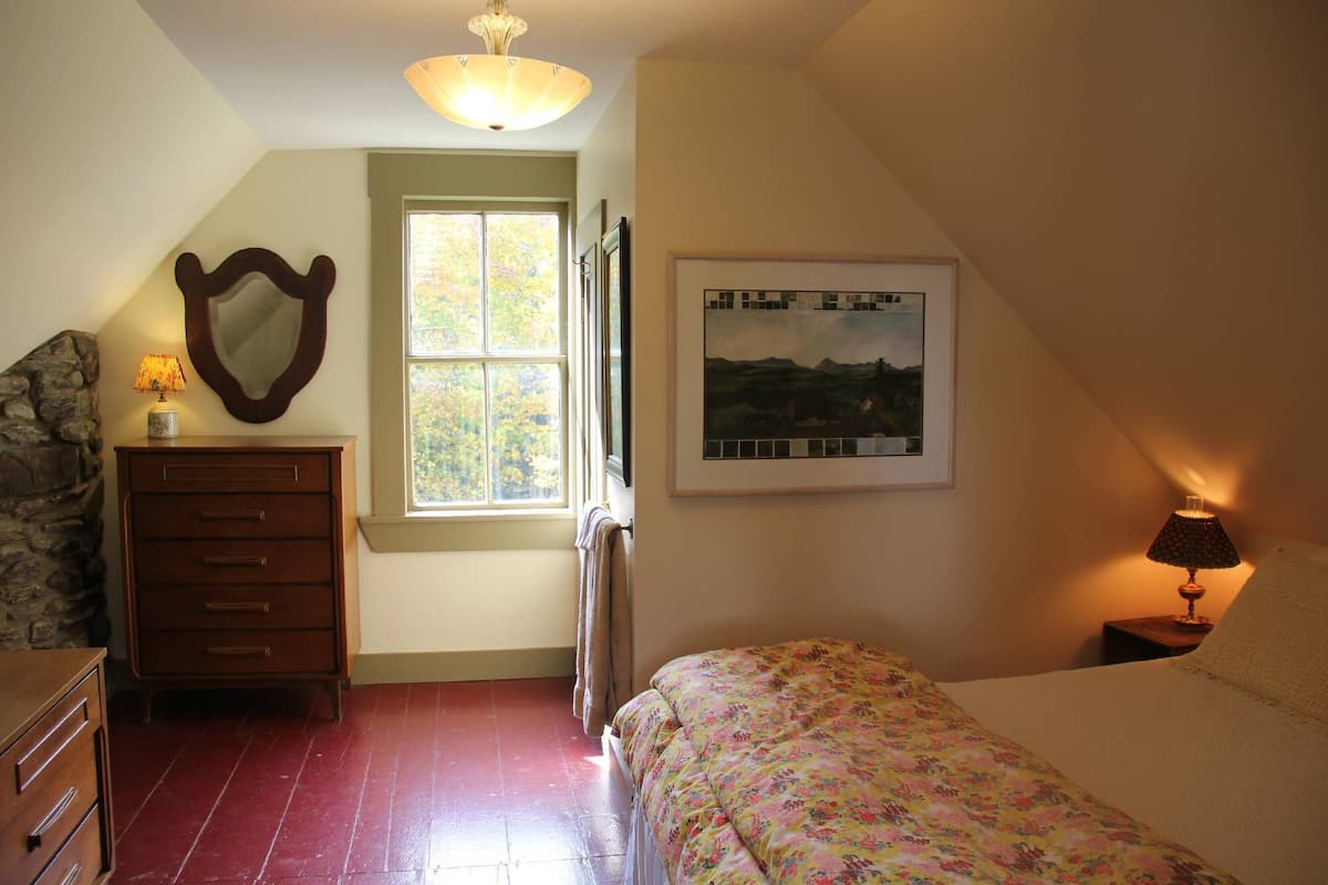 A bedroom with a bed, dresser, mirror, window, and artwork.