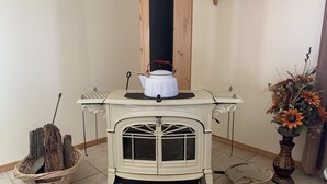 Un poêle à bois blanc avec une casserole dessus, un panier en osier rempli de bois de chauffage et un vase avec des fleurs.