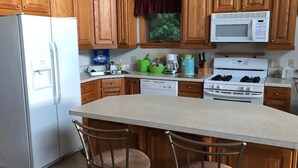 Una cocina con armarios de madera, un refrigerador blanco, un microondas, una estufa y un lavamanos. Hay dos taburetes de bar en la isla.