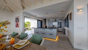 Une cuisine moderne dotée d’un îlot central, d’un coin repas avec des meubles en osier et d’une vue sur l’extérieur.