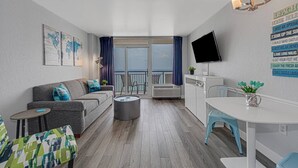 A modern living room with a grey sofa, a small round table, a TV mounted on the wall, and a balcony with a view. - Heavenly Oceanfront Relaxing Penthouse! (Myrtle Beach)