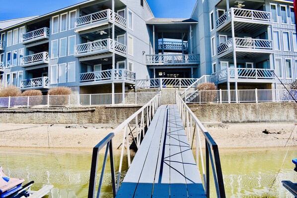 A multi-story building with balconies and a dock leading to a body of water.
