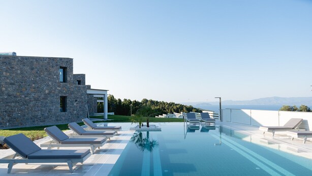 Un área de piscina moderna con sillones de descanso y un edificio de piedra.