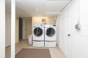 A laundry room with two front-loading washing machines, a small trash bin, and a door leading to another room.