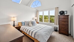 A bedroom with a bed, bedside tables, a dresser, a skylight, and a window with a view of greenery. - Beachfront Home-Fully Furnished.  PRIVATE Beach Rights on L.I. Sound. (Mt Sinai)