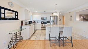 A modern kitchen with white cabinets, stainless steel appliances, and a glass island with bar stools. - Beachfront Home-Fully Furnished.  PRIVATE Beach Rights on L.I. Sound. (Mt Sinai)
