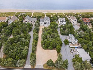 An aerial view of a residential area with houses, a central driveway, and a beach in the background.