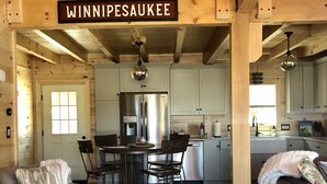 Ein gemütliches Blockhauss-Interieur mit Essbereich, Küche und Sitzgelegenheit. Ein Schild darüber zeigt den Schriftzug "WINNIPEAUKEE".