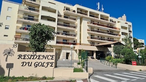 Un hôtel à plusieurs étages doté de balcons, une enseigne indiquant « RÉSIDENCE DU GOLF », et un palmier au premier plan.