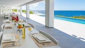 A dining area with a view of the ocean, white furniture, and a table set for a meal. - Villa 308 - Coral Estate (Rif. St. Marie)