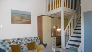 A modern living room with a geometric-patterned sofa, a dining table with a bowl of fruit, and a staircase leading to an upper level. - HOUSE WITH HEATED POOL CLOSE TO BEACHES AND NATIONAL FOREST (Saint-Jean-de-Monts, Vendée)