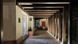 A covered corridor with wooden beams and brick flooring, leading to a red door at the end. - DETACHED HOUSE IN THE CENTER OF VALE DAS FURNAS  (Furnas)