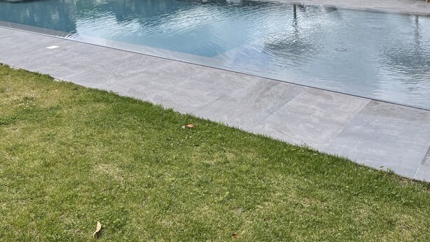 A swimming pool with lounge chairs and a stone wall, surrounded by a grassy area and mountains in the background. - DETACHED HOUSE IN THE CENTER OF VALE DAS FURNAS  (Furnas)