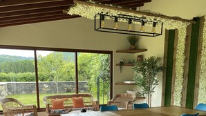 A dining area with a wooden table and blue chairs, surrounded by wicker chairs, with a view of greenery outside. - DETACHED HOUSE IN THE CENTER OF VALE DAS FURNAS  (Furnas)