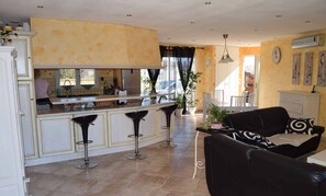 A spacious kitchen with a central island, bar stools, and a dining area with a sofa and chairs. - 3 bedroom VILLA with pool (Autignac)