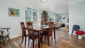 A dining area with a wooden table and chairs, a bookshelf, and a window with blinds. - Dog friendly one bedroom house close to everything! (Manistee)