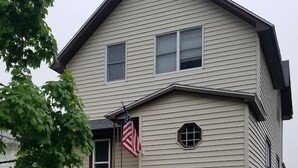 A two-story house with a front porch, a small garden, and an American flag. - Dog friendly one bedroom house close to everything! (Manistee)