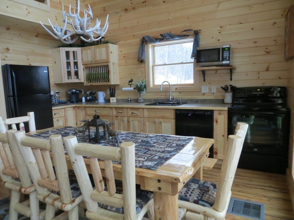 Interior de una cabaña de madera con una mesa de comedor, sillas, un refrigerador, un microondas, un lavabo y una estufa.