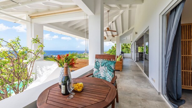 A covered outdoor seating area with a wooden table, a vase with flowers, and a view of the ocean. - Sugarbird Villa - Estate Coral (Rif. St. Marie)
