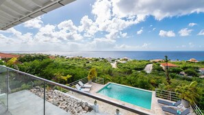 A pool with lounge chairs, surrounded by greenery and a view of the ocean. - Sugarbird Villa - Estate Coral (Rif. St. Marie)