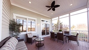 En overdækket terrasse med fletningsmøbler, et glasbord og en loftsvifte.