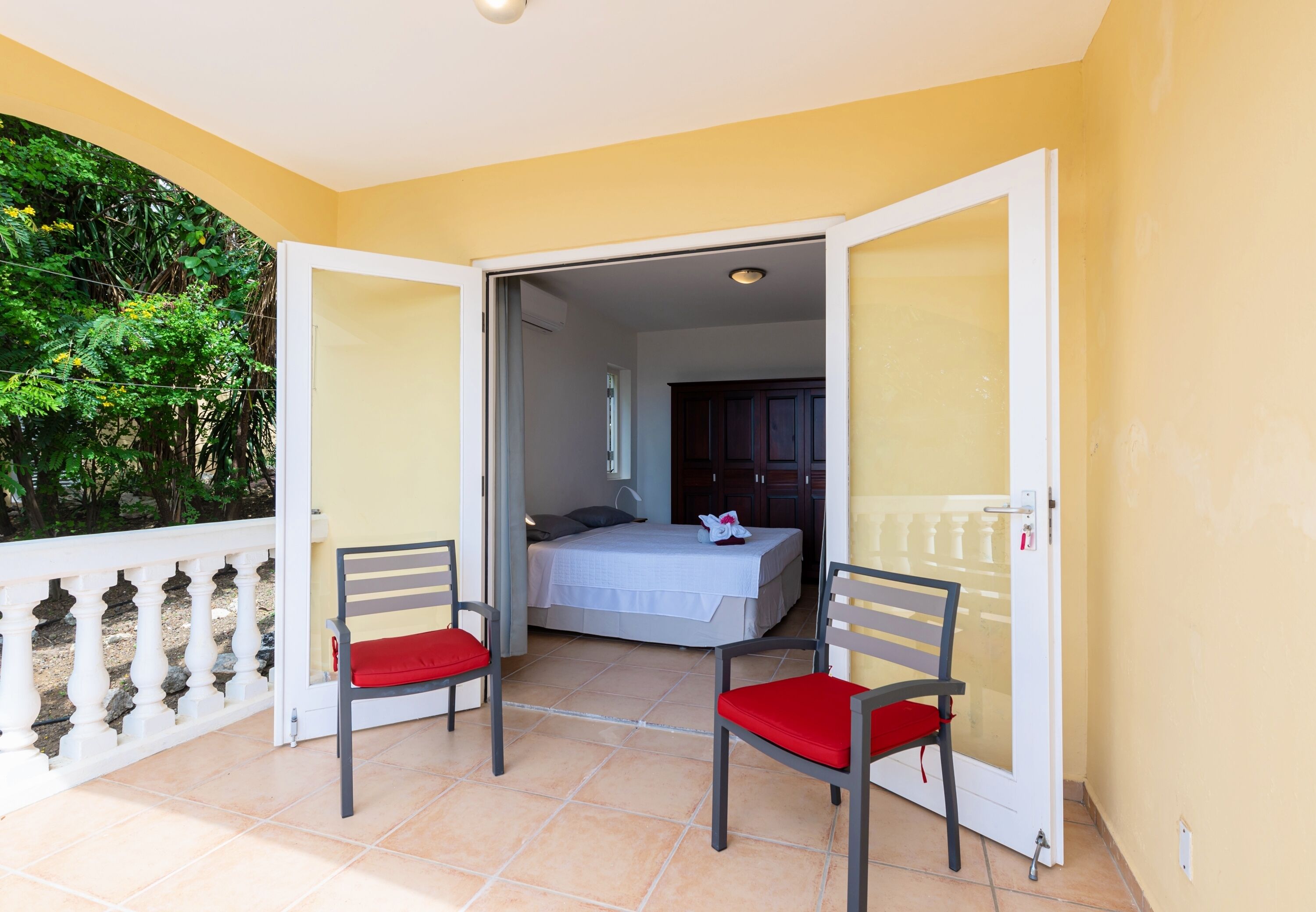 A balcony with two chairs, a bed, and a view of greenery.