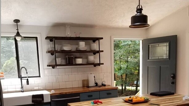 Una cocina moderna con una isla de madera, taburetes de bar y un estante empotrado sobre el fregadero.
