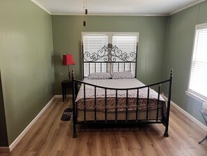 A bedroom with a bed, a nightstand, a lamp, and a window with blinds.