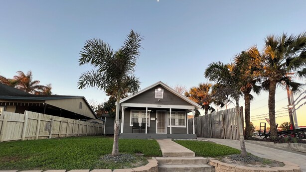 A residential house with a front porch, a stone retaining wall, and a driveway leading to the entrance. - Historic Downtown, Wifi, Apple TVs, Cold AC (Brownsville)