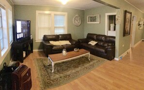 A living room with two dark leather couches, a wooden coffee table, a clock, and a television.
