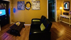 A living room with a leather sofa, a small table with a basket, a TV, and artwork on the walls. - Historic Downtown, Wifi, Apple TVs, Cold AC (Brownsville)