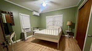 A bedroom with a single bed, a ceiling fan, an air conditioning unit, a desk with a chair, and a lamp. - Historic Downtown, Wifi, Apple TVs, Cold AC (Brownsville)